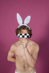 Funny naked guy wearing bunny ears over pink background