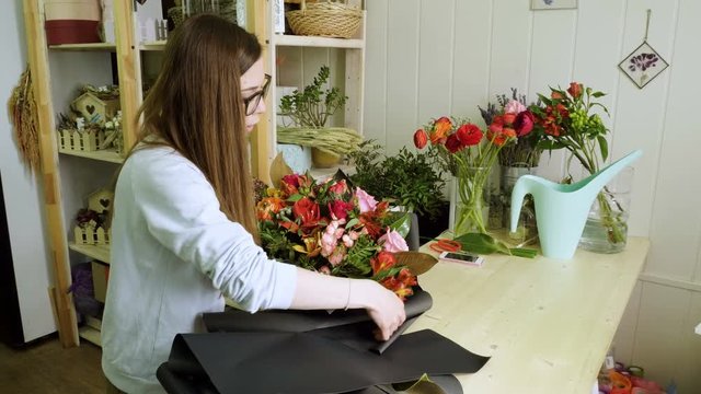 Female florist in flower shop. Woman making a beautiful and stylish bouquet of fresh flowers in floral design studio. 4K