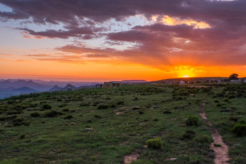 Sunset landscape over small village with mountains, clouds, orange sky and sun beams, Lesotho, Africa