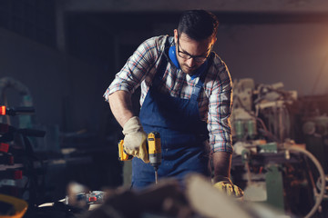 Carpenter drills a hole with an electrical drill 