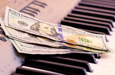 US Dollars lie on the piano keys. Payment for the concert, profit from performing musical works_