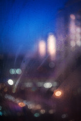 Blurred abstract background with lights of evening city through the misted window