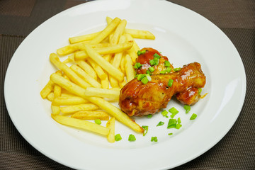 Fried potatoes with chicken legs and chopped green onions on a plate