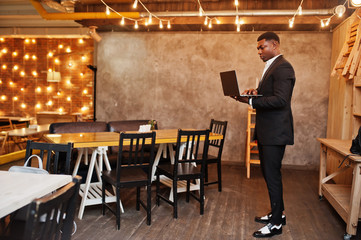Strong powerful african american man in black suit standing and working with laptop.