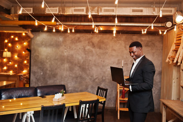Strong powerful african american man in black suit standing and working with laptop.