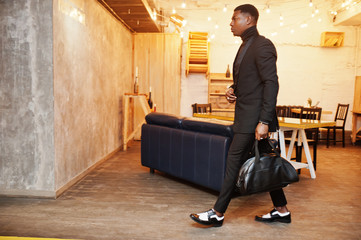 Strong powerful african american man in black suit and turtleneck with handbag posing in office.