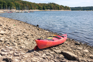 Einsames, rotes Kanu am Steinufer wartet auf seinen Einsatz im blauen, großen See