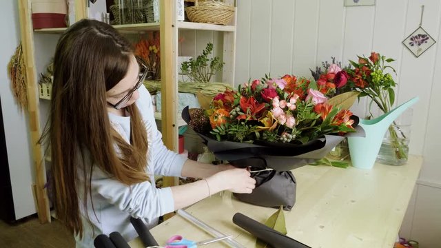 Female florist in flower shop. Woman making a beautiful and stylish bouquet of fresh flowers in floral design studio. 4K
