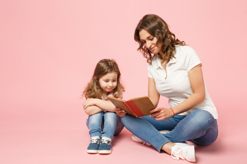 Woman in light clothes have fun read book with child baby girl. Mother, little kid daughter isolated on pastel pink background, studio portrait. Mother's Day, love family, parenthood childhood concept