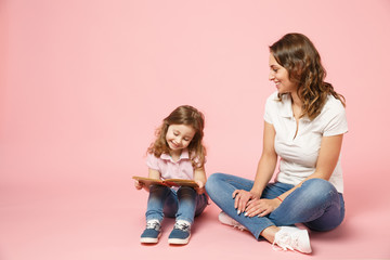 Woman in light clothes have fun read book with child baby girl. Mother, little kid daughter isolated on pastel pink background, studio portrait. Mother's Day, love family, parenthood childhood concept