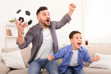 Father and son soccer fans cheering with football ball