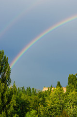 Natural double rainbow over green trees, summer city landscape
