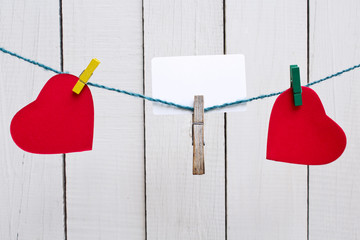 Hanging red heart shapes with blank card of white wooden background.