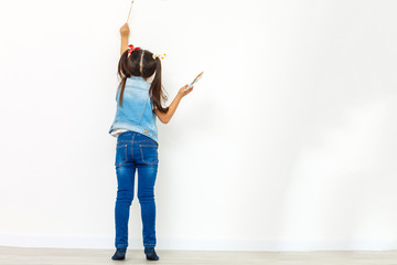Cute little girl painting on wall in empty room
