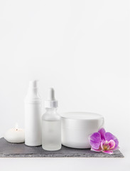 Obraz na płótnie Canvas Different material shape and size cosmetic product cream, oil containers on white background standing on black stone base, pink orchid blossom for decoration. Lot of copy space.