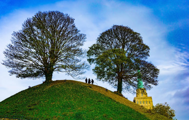 Two trees on the top of the castle mound with silhouette of three people on the top and the Spire...