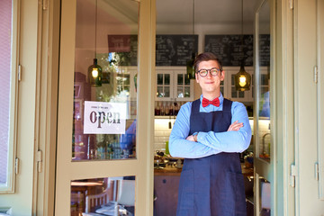 Small business owner young man standing in his cafe in the door