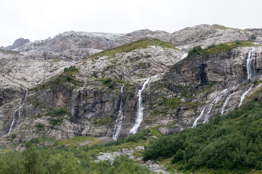 From the cloudy haze the summit peaks - Sofia, 3640m. On the slopes descend Sofia waterfalls, originating from the Sophia glacier. Arkhyz. KCR, Russia.
