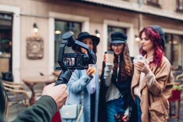 Obraz na płótnie Canvas Videographer filming models on city street. Man using steadicam and camera to make footage. Video shoot