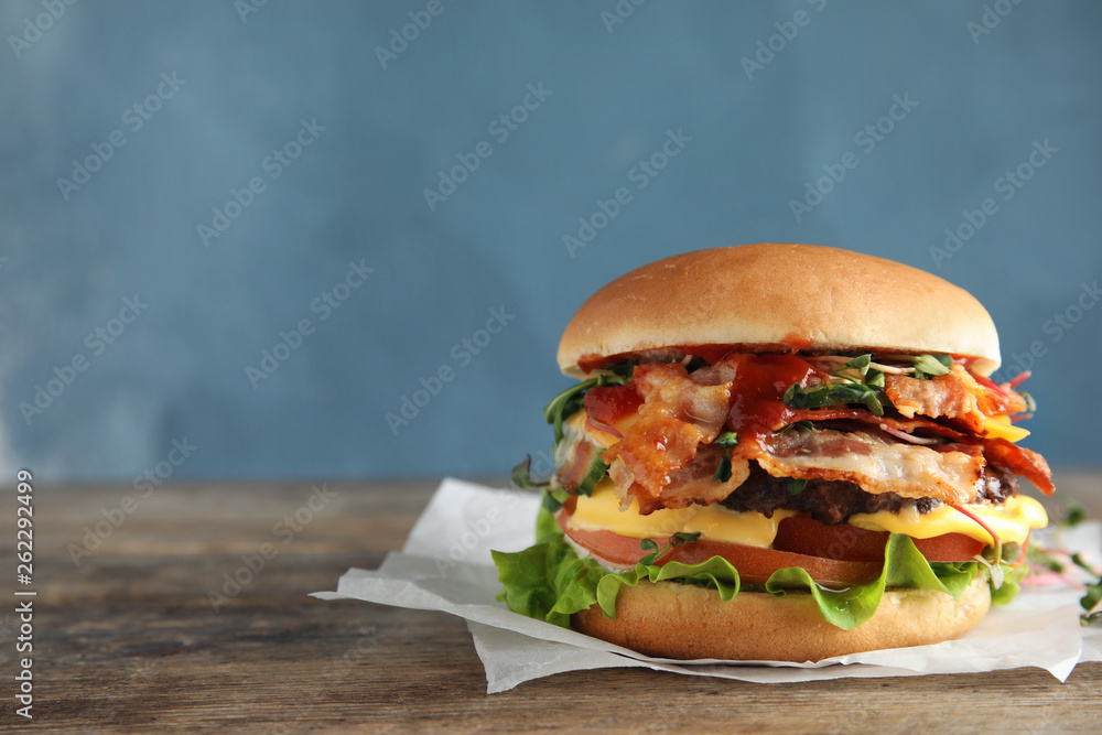 Wall mural Tasty burger with bacon on table against color background. Space for text