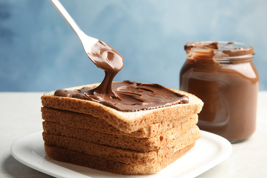 Spreading sweet chocolate cream onto toast on table against color background