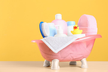 Baby cosmetic products, toy and towel on table against color background