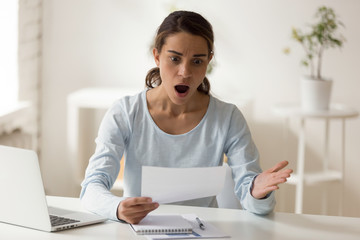 Shocked and confused woman looking at paper at desktop