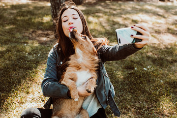 .Pretty young woman playing with her dog in the park outdoors. Taking pictures together doing funny funny faces with her mobile phone. Lifestyle. Dogfriendly.