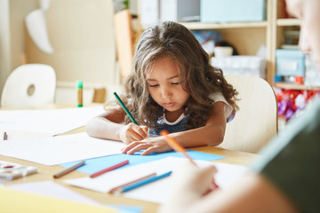 Focused girl with wavy hair sitting at table and drawing while attending art school