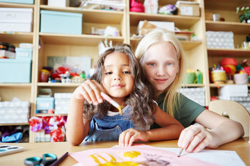 Two sweet little girls with paintbrushes smiling and looking at camera while painting during art...