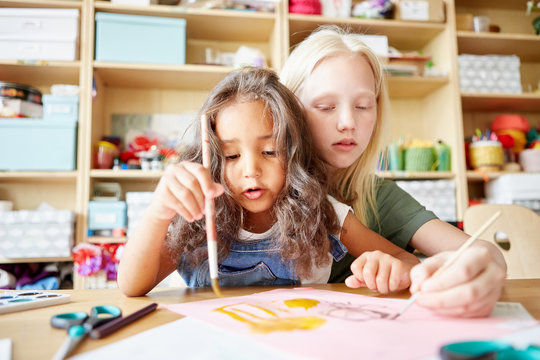 Two lovely little girls painting cute picture together while attending art class in school
