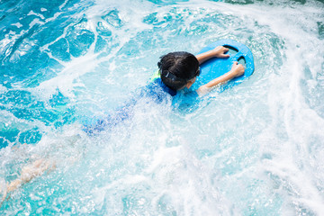 A boy is swimming with kickboard and swimming goggles.