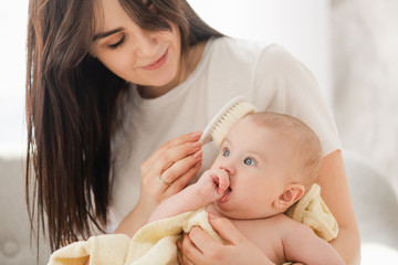 Smiling woman combing hair baby, close up.
