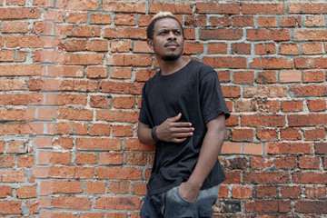 Young attractive dark-skinned man in black T-shirt on red bricked background.