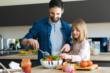 Attractive young man with her little cute daughter making salad together on kitchen at home