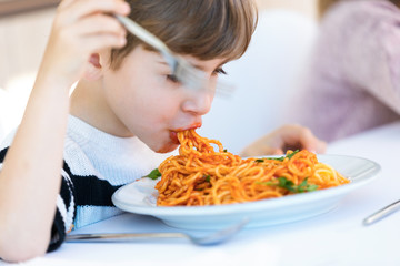 Hungry little boy eating spaghetti with tomato sauce in the kitchen at home.