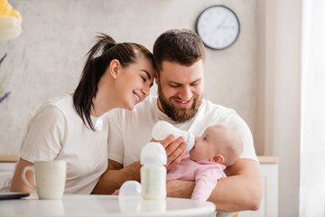 Happy young couple feeding infant from bottle - Powered by Adobe