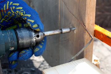 A carpenter working with an electric screwdriver repairing a wooden fence in protective gloves.