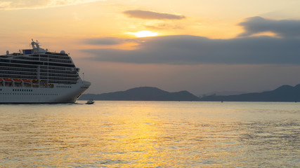 Fototapeta na wymiar Cruise liner starting voyage surrounded by beautiful sunset light and hills in the background