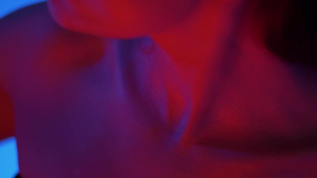 Close-up shot of collarbone and chin of futuristic and sexy fashion model in bright red neon lights in studio.