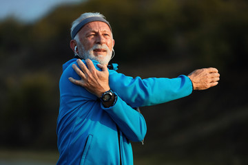 Senior sportsman stretching his arm while exercising in nature.