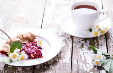 Cup of black fragrant tea and tasty piece of homemade strawberry cake on a on a wooden background jasmine branch. Place for text.