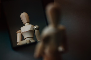 Loneliness. The figurine of a wooden man  stands in front of his reflection in the mirror. Conceptual image about psychological experiences. Emotional stress and pain.