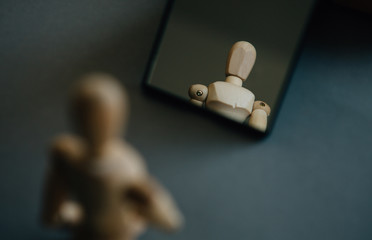 Loneliness. The figurine of a wooden man  stands in front of his reflection in the mirror....
