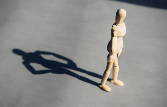 wooden man stands in front of the sun behind him, his shadow. The concept of personality, leadership.