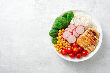 Fototapeta na wymiar Healthy buddha bowl with spinach, tomato, chickpea, rice, radish and grilled chicken on concrete background. Top view. Copy space.