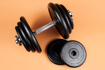 Obraz na płótnie Canvas Professional dumbbell and weight plates over beige background. Black metal dumbbell with chrome silver handle. Gym equipment. Fitness concept.