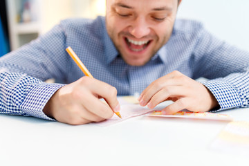 Photo of happy man with lottery ticket and pencil sitting at table