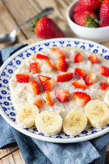 Oatmeal Porridge with Strawberries and banana on wooden rustic table. Healthy Breakfast with Fresh Organic Berries.