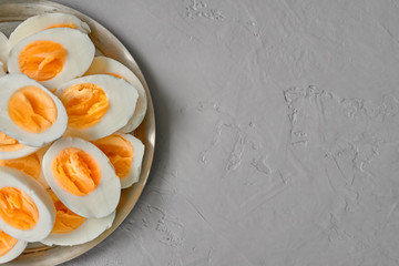Boiled eggs sliced on wooden cutting board over gray concrete background Top view